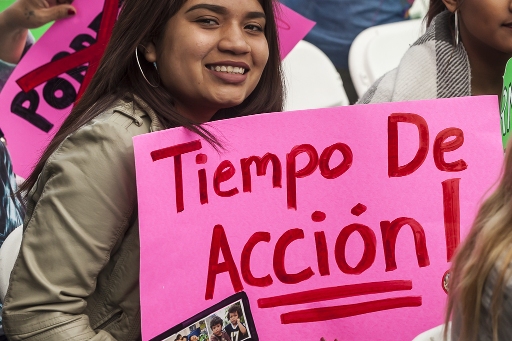 An adolescent with brown hair smiles as she holds up a sign that reads, "Tiempo de Accion" or "Time for Action."