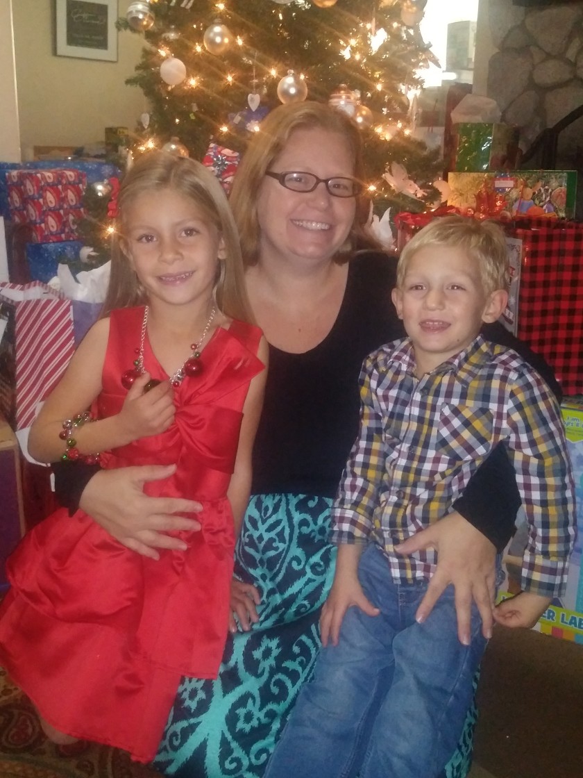 Childcare provider Jessica Sommerville sits in front of a Christmas tree with two children on her lap