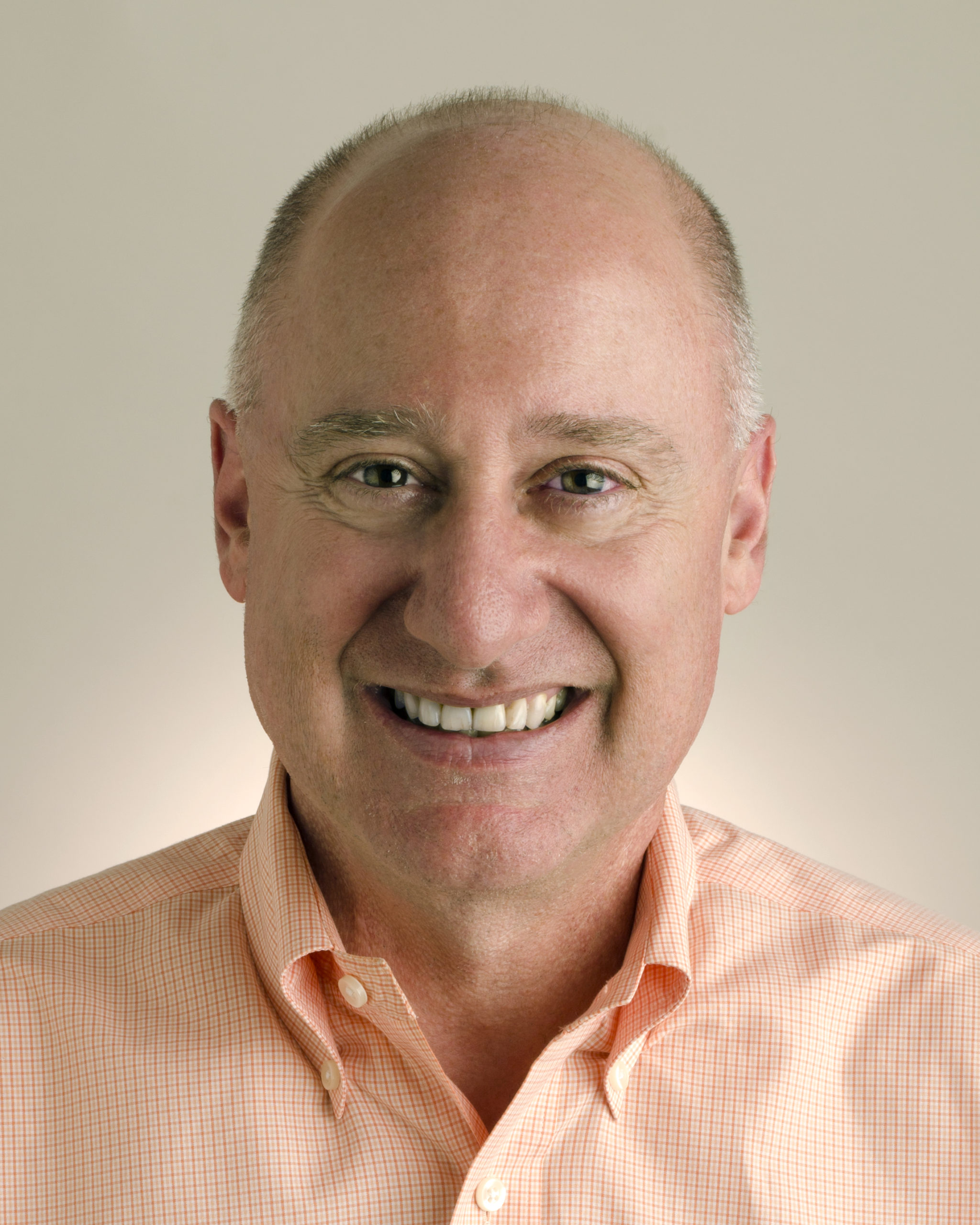 A photograph of Ted Lempert in an organge shirt against a beige background.